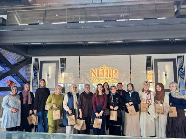 Görselde, basın etkinliği sırasında bir grup kadın, kurumsal etkinlik alanında bulunan NEHIR Çikolata logosu önünde birlikte duruyor.