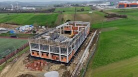 Yapım aşamasında olan modern bina, inşaat sürecinde ve çevresinde yeşil alanlar.