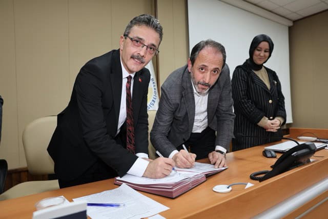 Üç kişi, masada anlaşma imzalarken, resmi ortamda toplantı yapıyor.